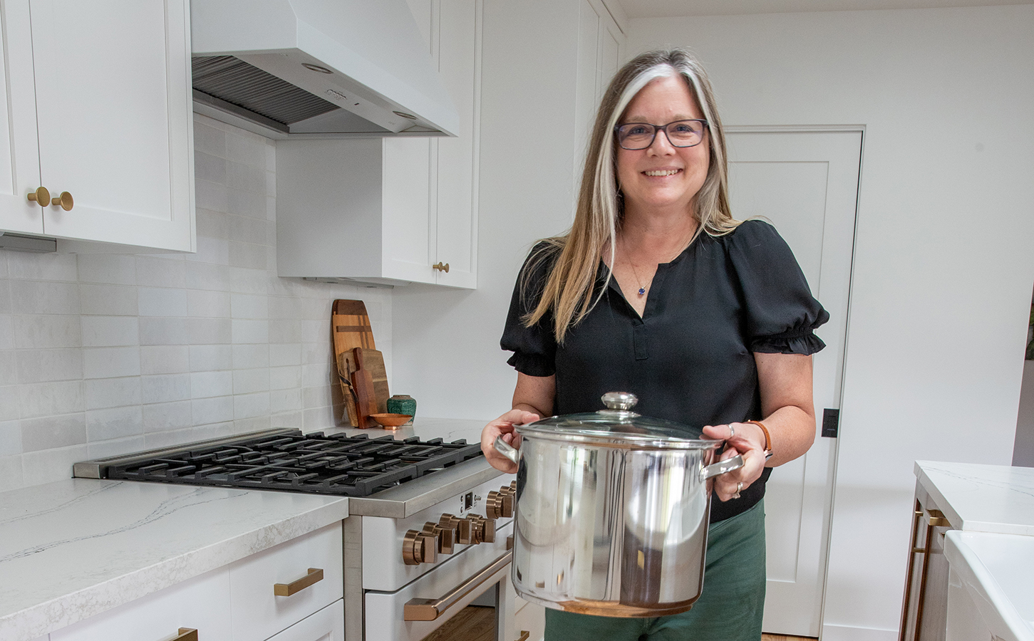 Nancy Ingersoll holding a pot in a white modern kitchen with professional range
